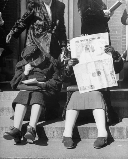 Women reading newspapers while waiting in line for matinee perfo